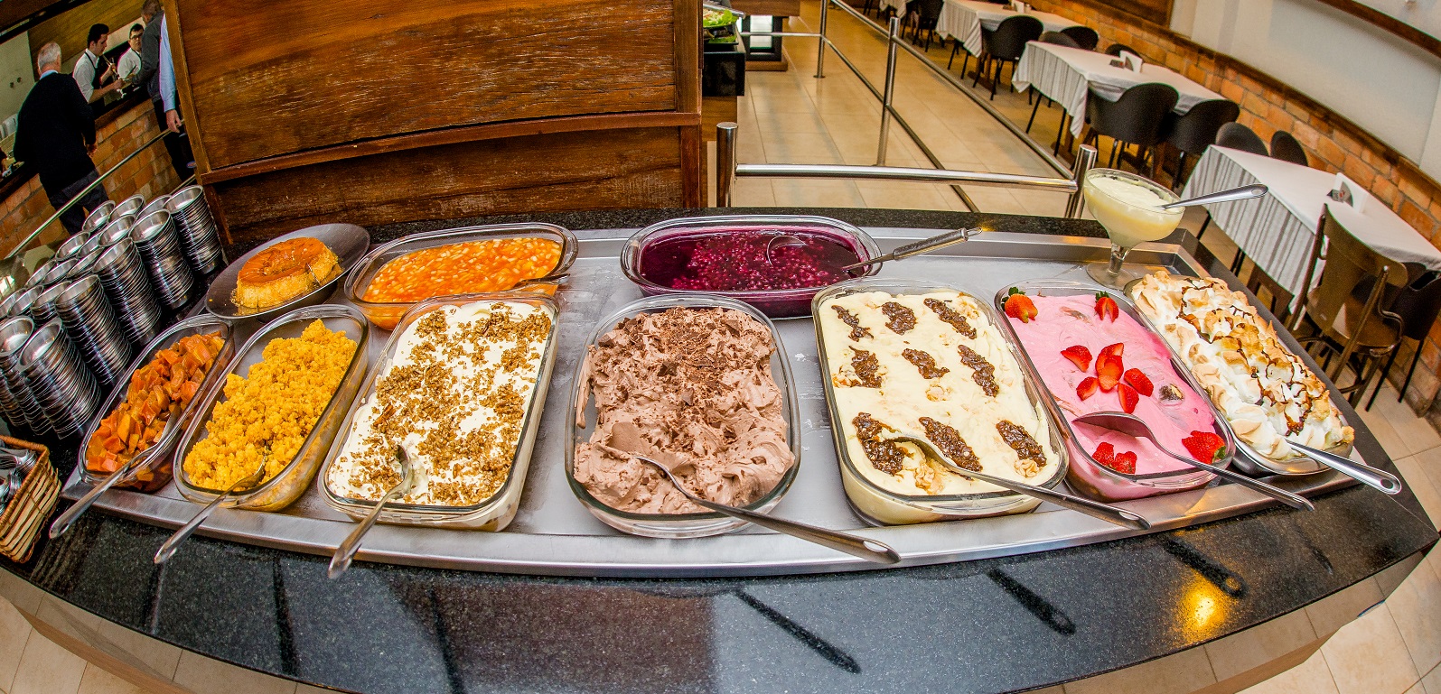 Mesa de sobremesas do buffet, com o salão ao fundo.